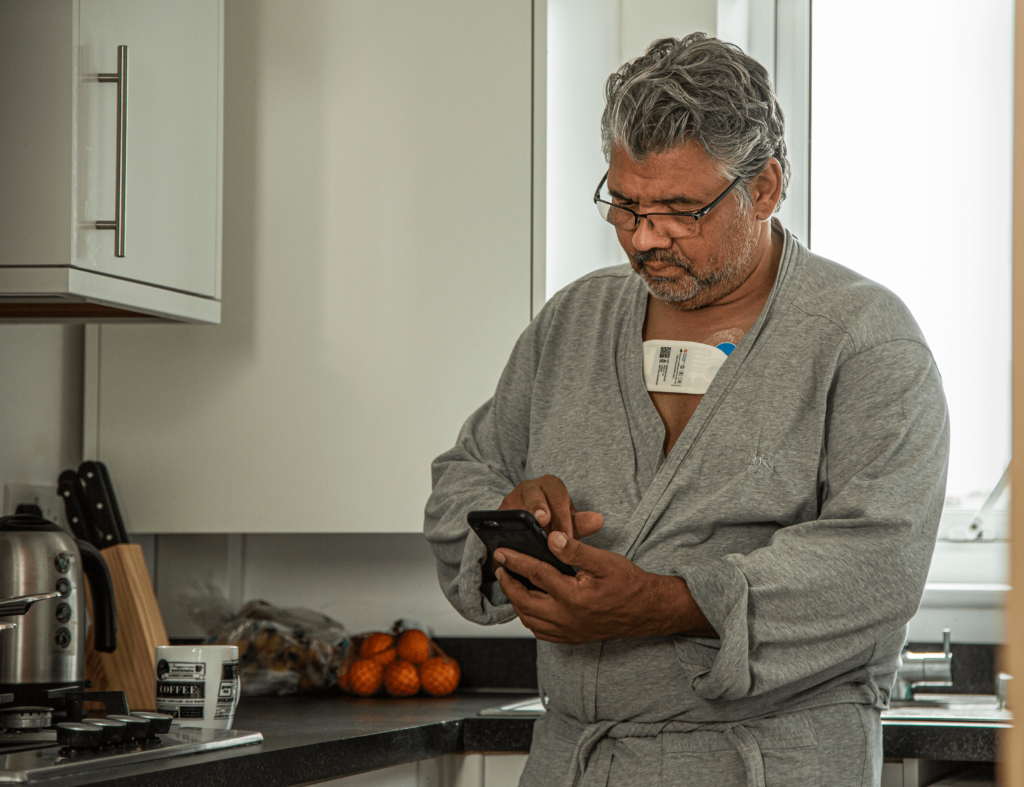 Man with Sensium patch in kitchen with mobile phone